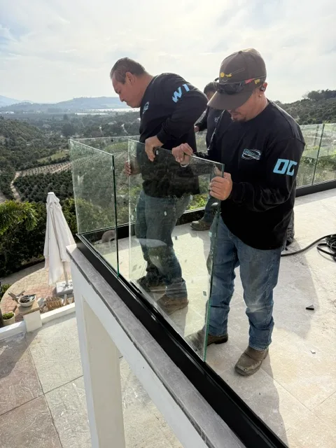 Two pros installing a frameless glass railing on a hillside deck